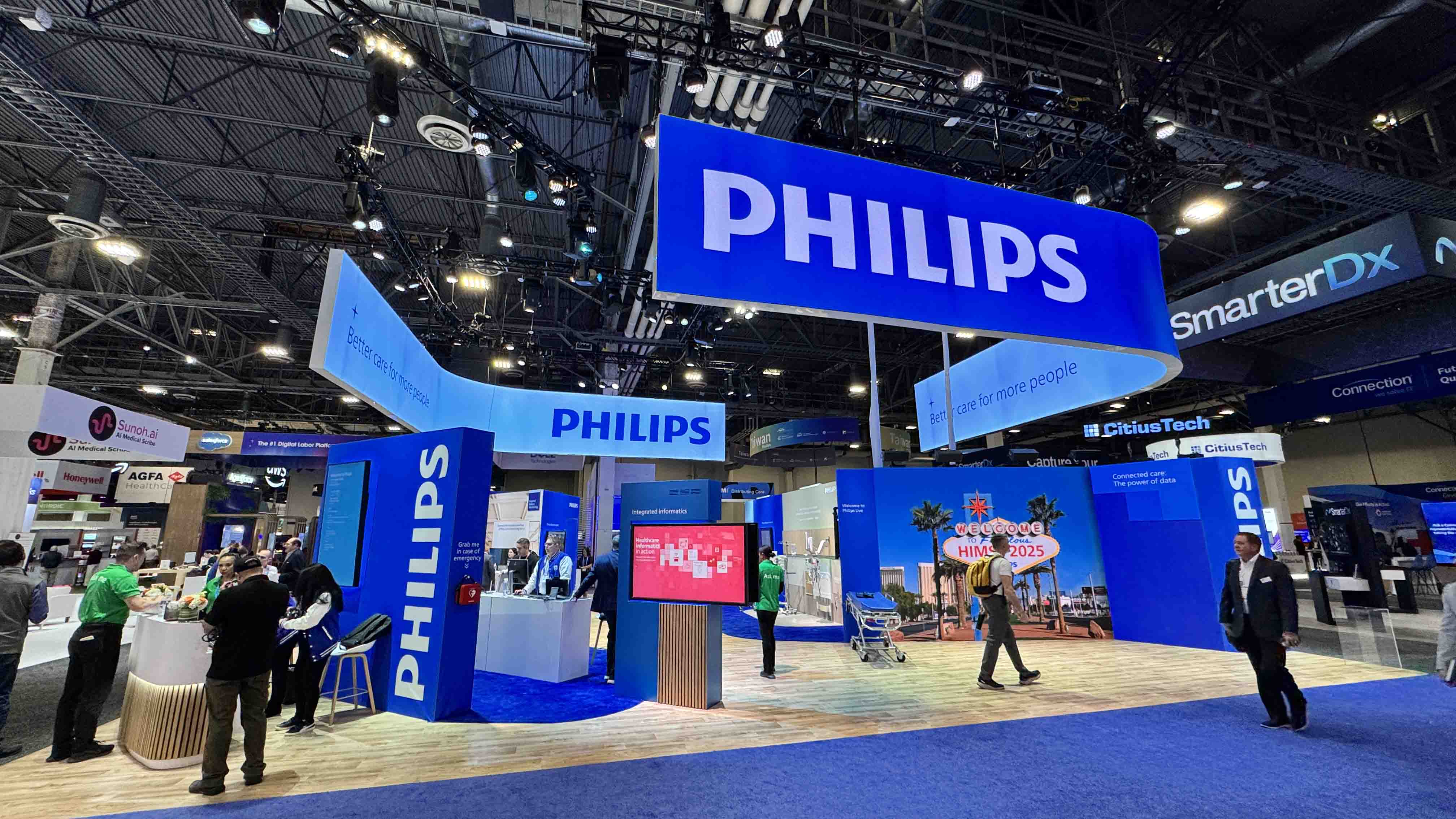 An image of a tradeshow booth. The booth is blue in color and has several large screens. The booth is Owned by Philips